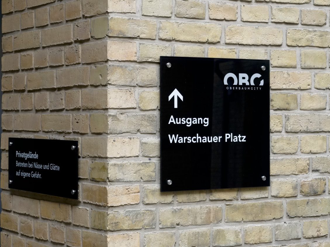 Planung Richtungsschilder Hof Oberbaumcity Berlin Friedrichshain Schwarzes Hinweisschild an Klinkerwand im Hof für einen Ausgang, Pfeil Richtung nach oben.