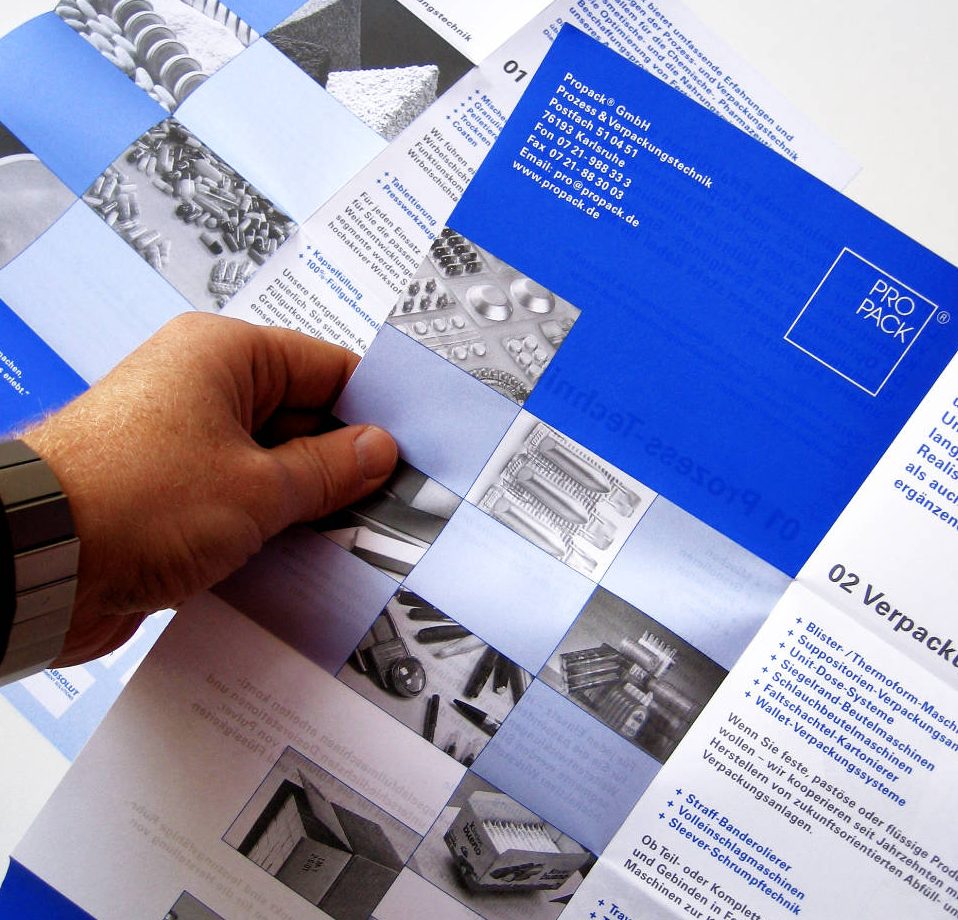 Broschürendesign und Corporate Design Propack Prozess- und Verpackungstechnik Karlsruhe Eine Hand hält einen Flyer mit blauen quadratischen Flächen und Bildern.