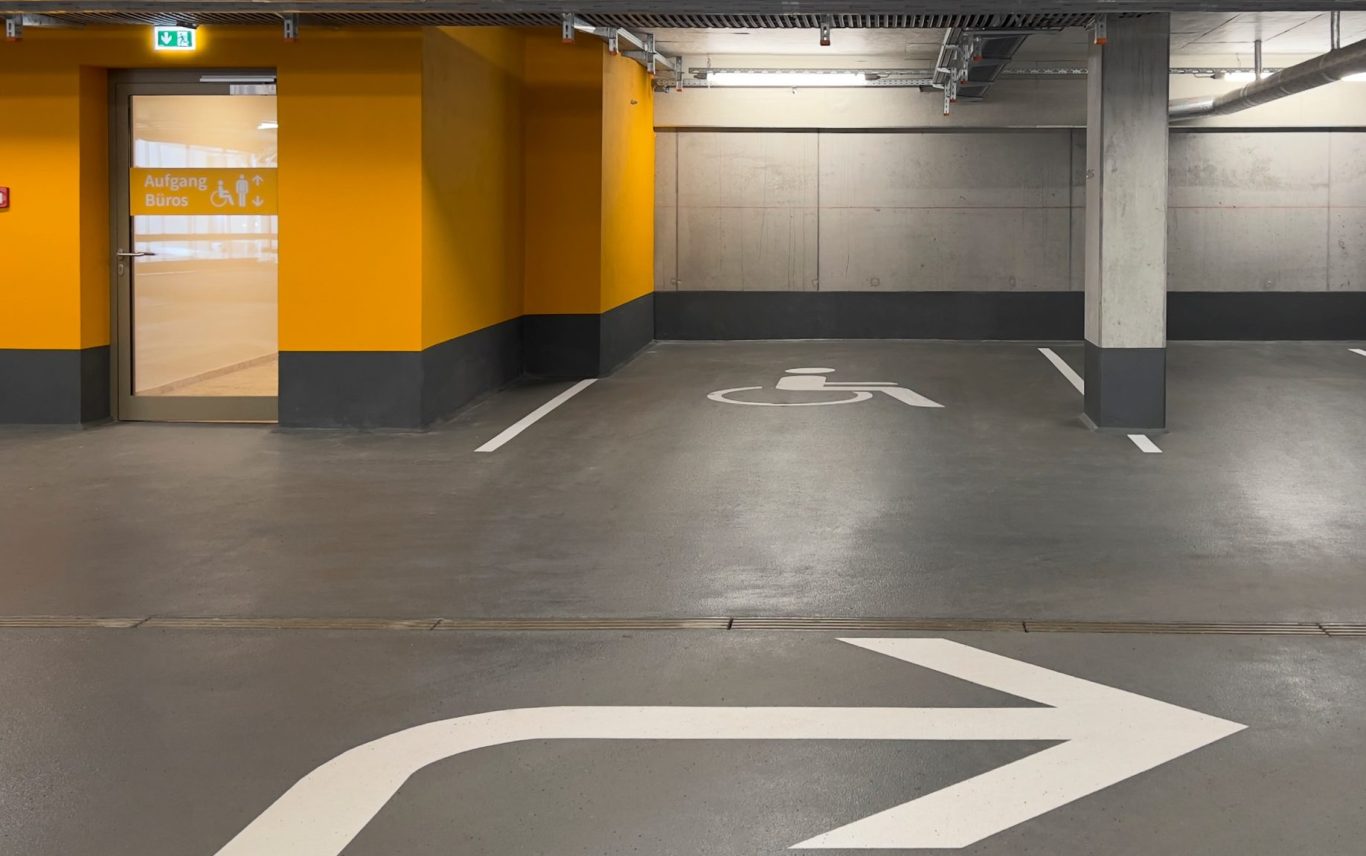 Planung Wegeleitsystem Parkgarage Bürohaus Schönefeld Parkgaragenfahrbahn mit gelber Wand und einem Pfeil nach rechts.