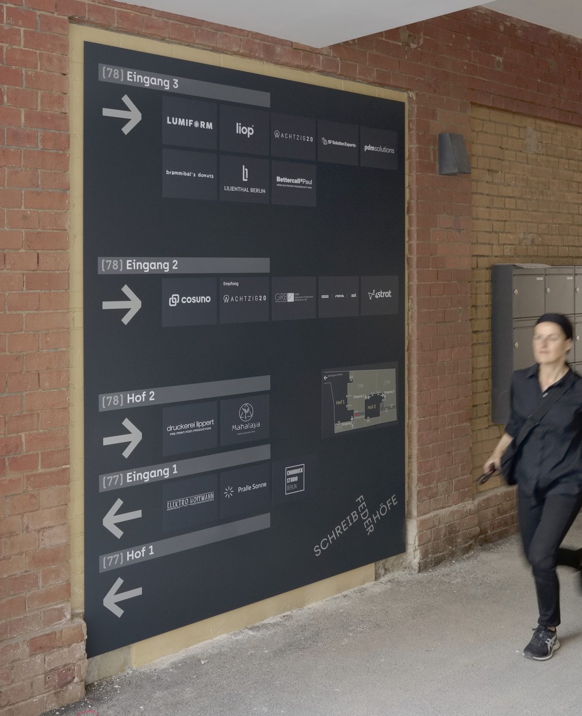 Gestaltung Mieterübersicht für Hof Schreibfederhöfe Berlin Dunkelgraue Wandtafel im Hofdurchgang mit Wegweisern und Lageplan, Person läuft daran vorbei.